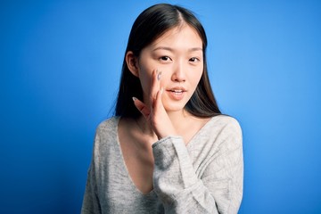 Young beautiful asian woman wearing casual sweater standing over blue isolated background hand on...