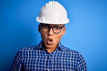 Young handsome engineer latin man wearing safety helmet over isolated blue background afraid and shocked with surprise expression, fear and excited face.