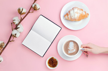 Hands holding coffee and notebook with croissant and cotton branch