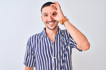 Young handsome man wearing nautical striped shirt standing over isolated background doing ok gesture with hand smiling, eye looking through fingers with happy face.