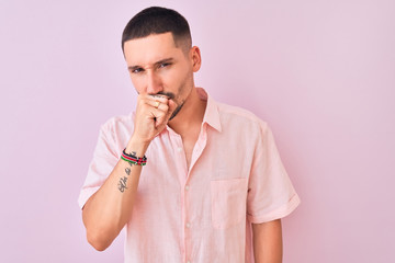 Young handsome man wearing pink shirt standing over isolated background feeling unwell and coughing...