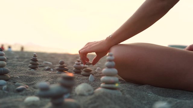 Woman practicing yoga on the beach. Balance ang relax. Tanned slim girl collects stones. Relaxation and yoga exercises on the beach.