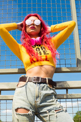 Urban portrait of a girl with red hair, a yellow T-shirt and ripped jeans, pink headphones, listens...