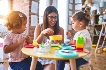 Young beautiful teacher and toddlers playing meals using plastic food and cutlery toy at kindergarten