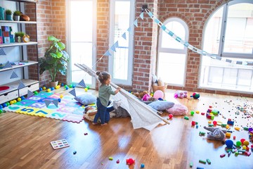 Adorable toddlers playing with tipi around lots of toys at kindergarten