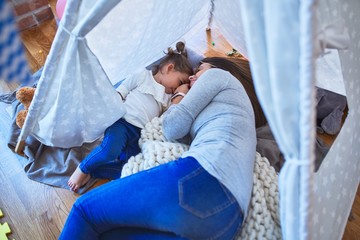 Young beautiful teacher and toddler smiling with happy face lying down over blanket inside tipi at kindergarten © Krakenimages.com