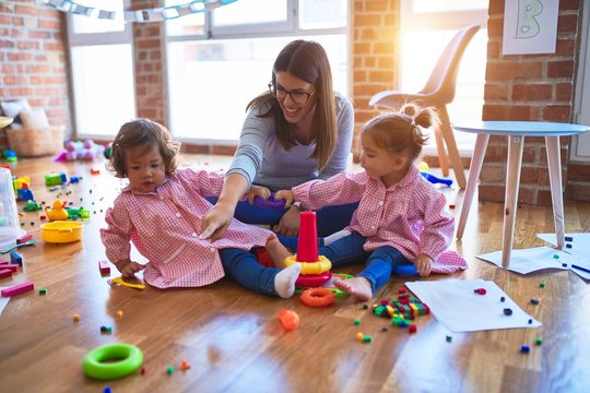 Young beautiful teacher and toddlers wearing uniform building pyramid using hoops at kindergarten