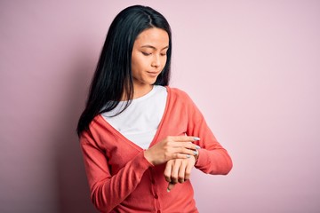 Young beautiful chinese woman wearing casual sweater over isolated pink background Checking the time on wrist watch, relaxed and confident