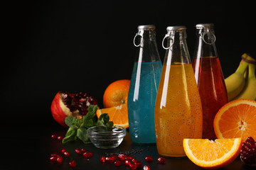 Trendy tropical, orange and pomegranate juice with basil seeds in bottles on black background, Closeup