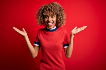 Young beautiful african american woman wearing casual t-shirt standing over red background celebrating crazy and amazed for success with arms raised and open eyes screaming excited. Winner concept