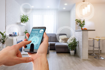 Smart home technology interface on smartphone app screen with augmented reality (AR) view of internet of things (IOT) connected objects in the apartment interior, person holding device - Powered by Adobe