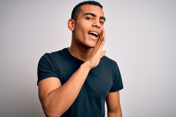 Young handsome african american man wearing casual t-shirt standing over white background hand on mouth telling secret rumor, whispering malicious talk conversation