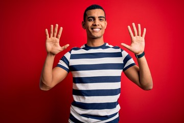 Naklejka premium Handsome african american man wearing casual striped t-shirt standing over red background showing and pointing up with fingers number ten while smiling confident and happy.