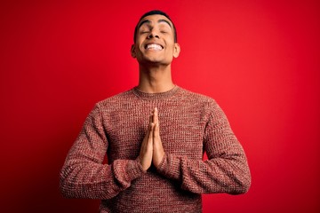 Young handsome african american man wearing casual sweater standing over red background begging and...