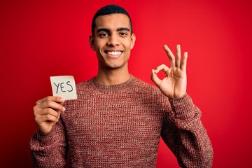 Young handsome african american man holding reminder paper with yes message doing ok sign with...