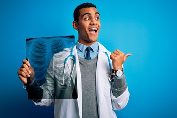 Handsome african american doctor man wearing stethoscope holding chest xray pointing and showing with thumb up to the side with happy face smiling