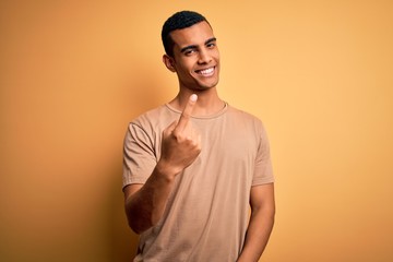 Young handsome african american man wearing casual t-shirt standing over yellow background Beckoning come here gesture with hand inviting welcoming happy and smiling