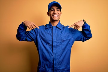 Young african american mechanic man wearing blue uniform and cap over yellow background looking...