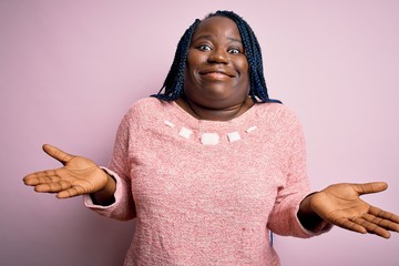 African american plus size woman with braids wearing casual sweater over pink background clueless...