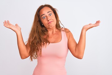 Middle age mature woman standing over white isolated background clueless and confused expression with arms and hands raised. Doubt concept.