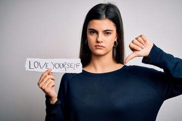 Young beautiful woman asking for take care of you holding paper with love yourself message with...