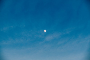 The moon in the middle of the photograph with the blue sky of a sunny day