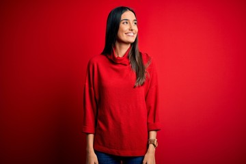 Young beautiful brunette woman wearing casual sweater over isolated red background looking away to...