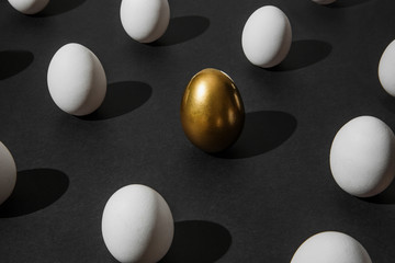 White and gold chicken eggs in vertical position on plain black paper background. Creative...