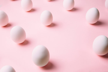 White chicken eggs nicely arranged in creative pattern on pastel pink background. Creative Ester holiday concept.
