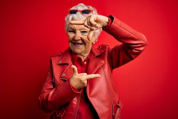 Senior beautiful grey-haired woman wearing casual red jacket and sunglasses smiling making frame with hands and fingers with happy face. Creativity and photography concept.