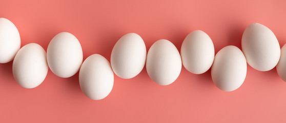 White chicken eggs arranged in a row on pastel pink backcground. Abstract Easter concept.