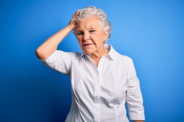 Senior beautiful woman wearing elegant shirt standing over isolated blue background confuse and wonder about question. Uncertain with doubt, thinking with hand on head. Pensive concept.