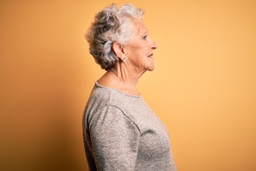 Senior beautiful woman wearing casual t-shirt standing over isolated yellow background looking to...