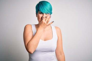 Young beautiful woman with blue fashion hair wearing casual t-shirt over white background smelling...