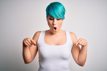 Young beautiful woman with blue fashion hair wearing casual t-shirt over white background Pointing down with fingers showing advertisement, surprised face and open mouth