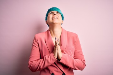 Young beautiful businesswoman with blue fashion hair wearing jacket over pink background begging...