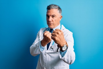 Middle age handsome grey-haired doctor man wearing coat and blue stethoscope Ready to fight with...