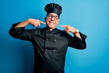 Middle age handsome grey-haired chef man wearing cooker uniform and hat smiling cheerful showing and pointing with fingers teeth and mouth. Dental health concept.