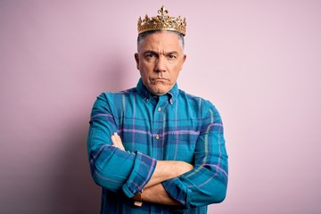 Middle age handsome grey-haired man wearing golden crown of king over pink background skeptic and nervous, disapproving expression on face with crossed arms. Negative person.