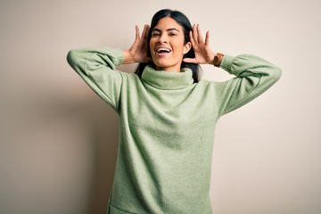 Young beautiful hispanic woman wearing green winter sweater over isolated background Smiling cheerful playing peek a boo with hands showing face. Surprised and exited