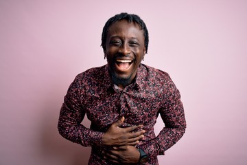 Young handsome african american man wearing casual shirt standing over pink background smiling and laughing hard out loud because funny crazy joke with hands on body.