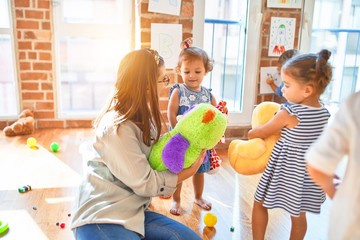 Obraz premium Beautiful teacher and group of toddlers playing around lots of toys at kindergarten