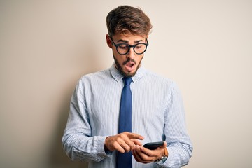 Young businessman having a conversation using smartphone over white background scared in shock with...