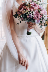 Close up of bride's hands holding modern a beautiful, stylish wedding bouquet of purple, pink roses and eucalyptus greenery. Summer floral composition.