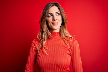 Fototapeta premium Young beautiful brunette woman wearing casual turtleneck sweater over red background smiling looking to the side and staring away thinking.
