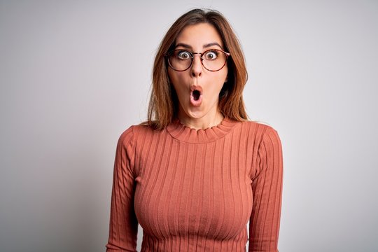 Young beautiful brunette woman wearing casual sweater and glasses over white background afraid and shocked with surprise expression, fear and excited face.