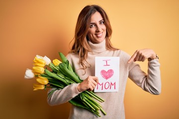 Beautiful brunette woman holding love mom message and tulips celebrating mothers day very happy pointing with hand and finger