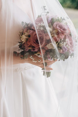 Bride's hands holding modern a beautiful, stylish wedding bouquet of purple, pink roses and eucalyptus greenery. Summer floral composition.