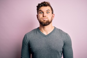 Young handsome blond man with beard and blue eyes wearing casual sweater puffing cheeks with funny face. Mouth inflated with air, crazy expression.