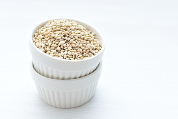 Raw barley grains, released in containers on white wooden background